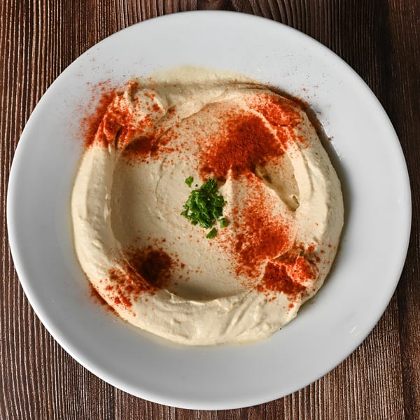 Creamy hummus topped with red paprika and green parsley, served on a white plate.