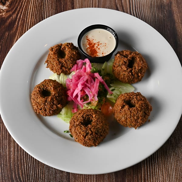 Five falafel pieces with pickled pink turnips, lettuce, and a side of tahini sauce.