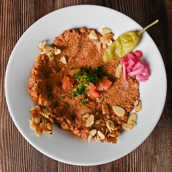 Kabobji's kibbeh nayyeh, a Middle Eastern dish, garnished with almonds, tomatoes, parsley, and pickled vegetables.