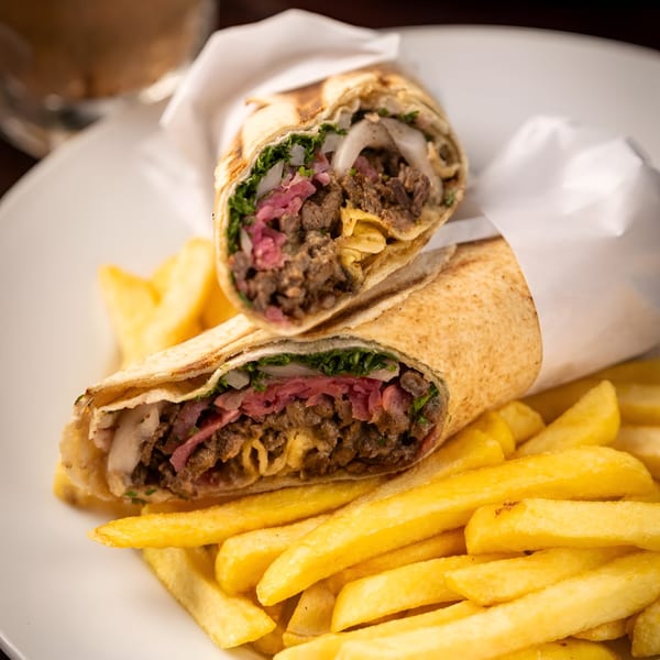 Two beef shawarma wraps with pickled red cabbage, onions, and fries on a white plate.