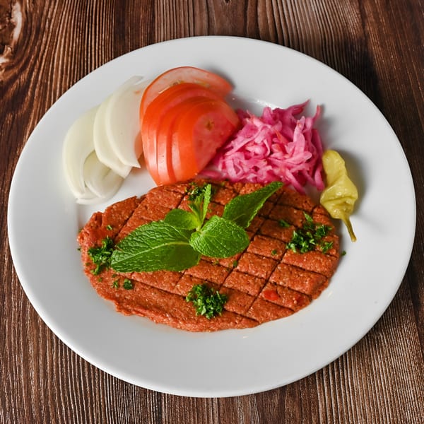 Kabobji's kibbeh nayyeh, a raw meat dish, garnished with mint, parsley, and served with pickled vegetables.