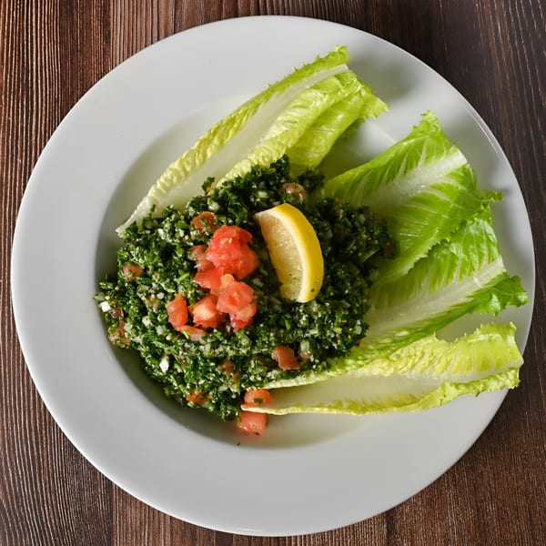 A white plate of Kabobji's tabbouleh salad with lettuce, tomatoes, and a lemon wedge.