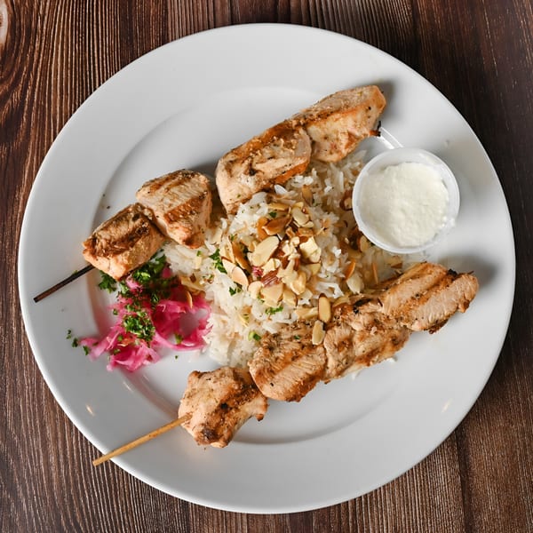 Kabobji's chicken shish tawook with rice, almonds, pickled turnips, and garlic sauce on a white plate.